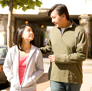 A father and his teenaged daughter walking down a street having a conversation.